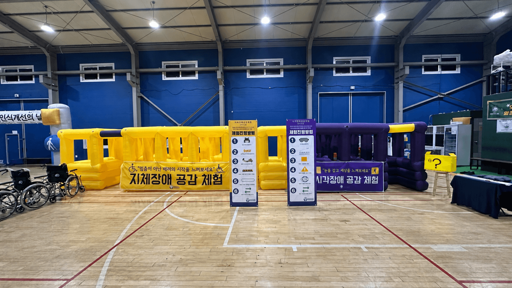 행복한길잡이 체험교육 현장 — 지체장애 공감 체험(휠체어)과 시각장애 공감 체험 부스가 설치된 체육관