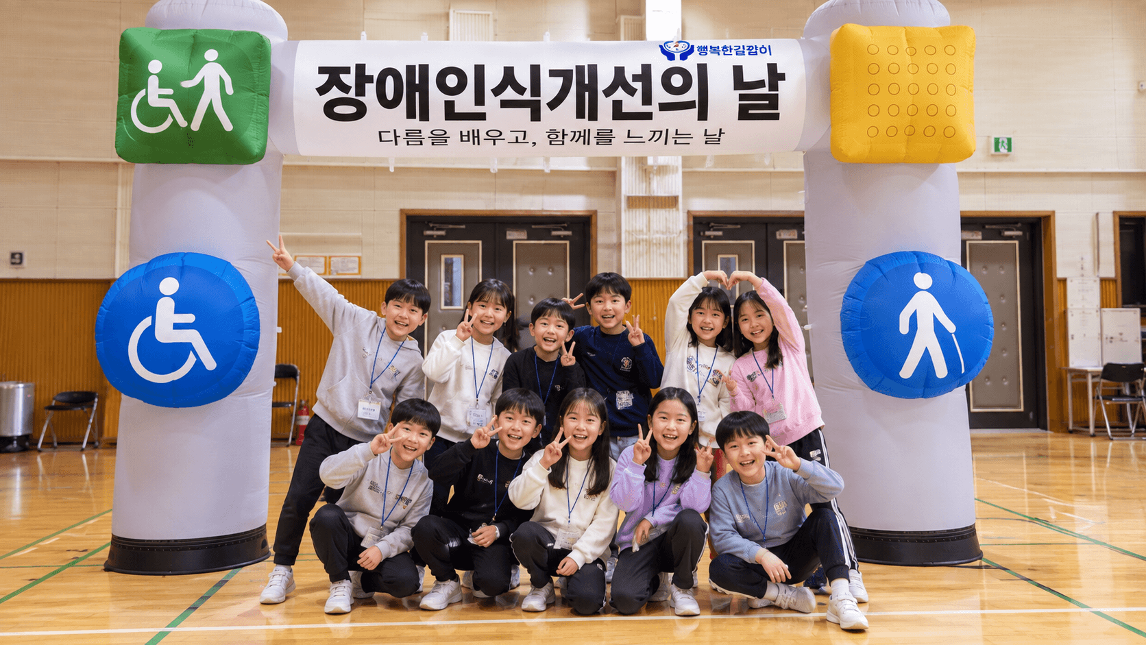 장애인식개선의 날 행사장 아치 아래 모인 초등학생들이 밝게 웃으며 브이 포즈를 하고 있다